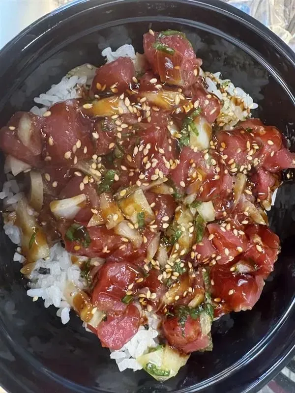 Poke bowl with diced tuna, sesame seeds, and sauce over rice.
