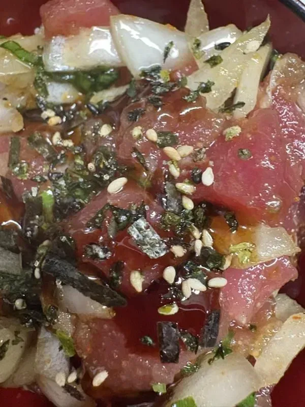 Close-up of ahi poke bowl with red tuna, white onions, seaweed, sesame seeds, and sauce.