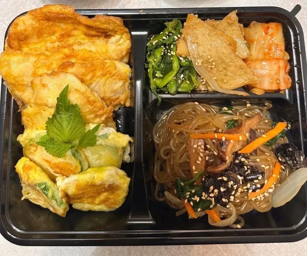 Korean bento box: fried pancakes, seasoned spinach, glass noodles, tofu, kimchi.