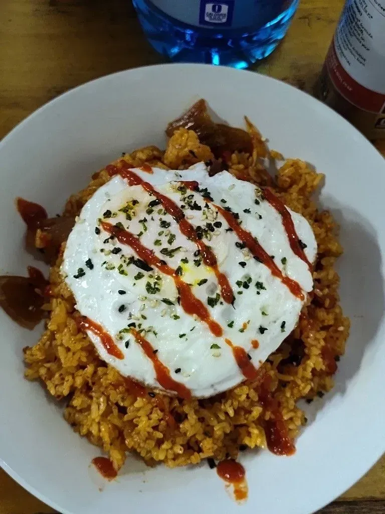 Fried rice topped with a fried egg, drizzled with sauce, and garnished.