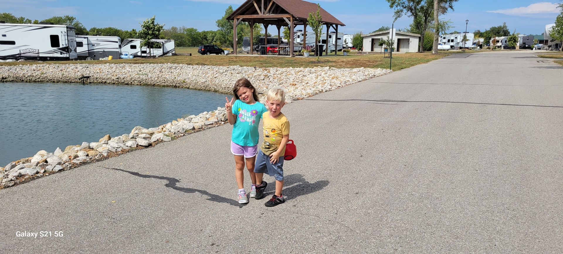 A boy and a girl are standing next to each other in front of a lake.