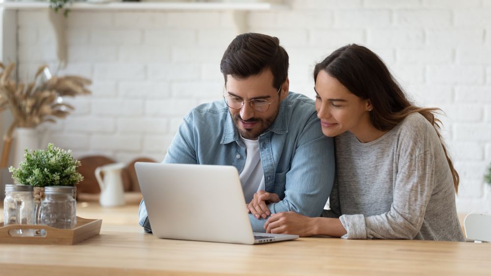 A man and a woman are sitting at a table looking at a laptop computer.