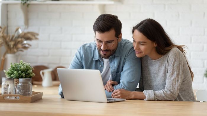 A man and a woman are sitting at a table looking at a laptop computer.