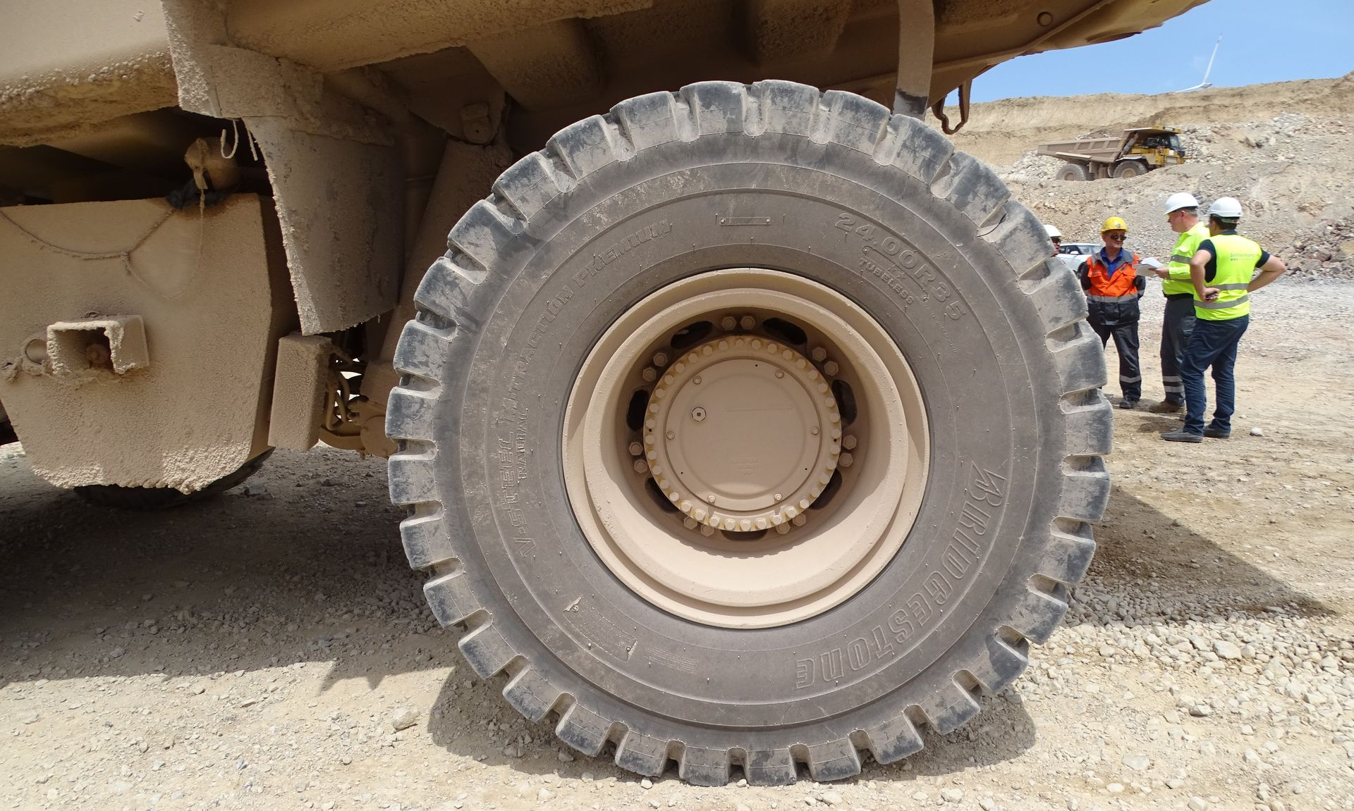 Large truck tire in a quarry; workers in safety vests stand nearby.
