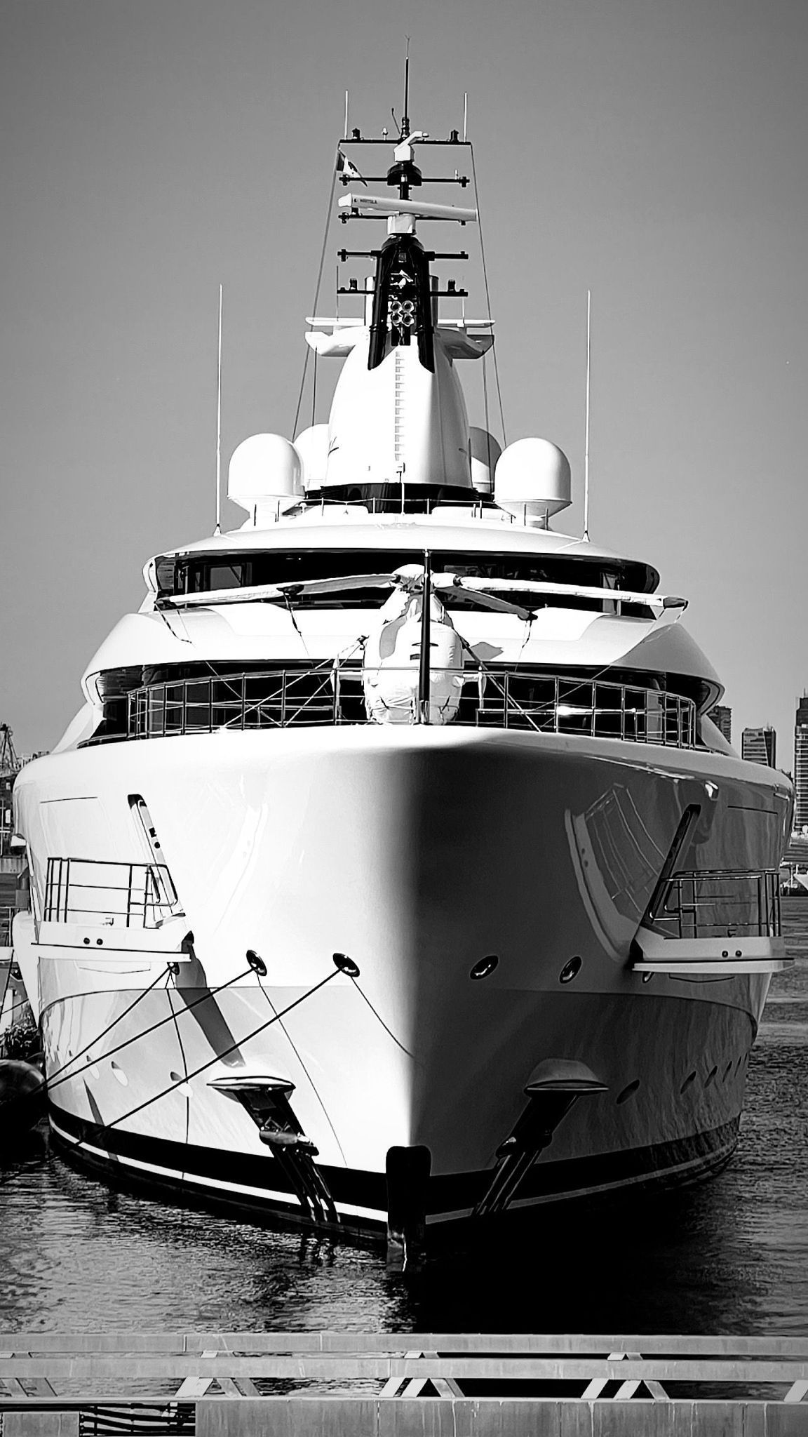 A front-facing view of a large, modern white yacht docked at a harbor under a clear sky.