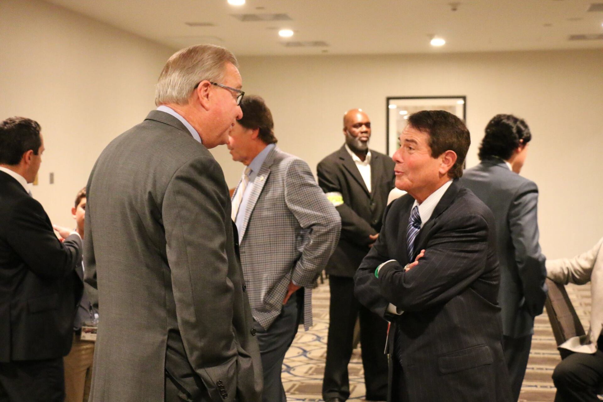 A group of men in suits are standing in a room talking to each other.