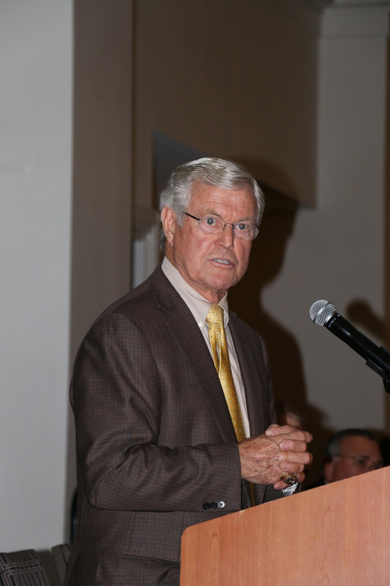 A man in a suit and tie is standing at a podium with a microphone.
