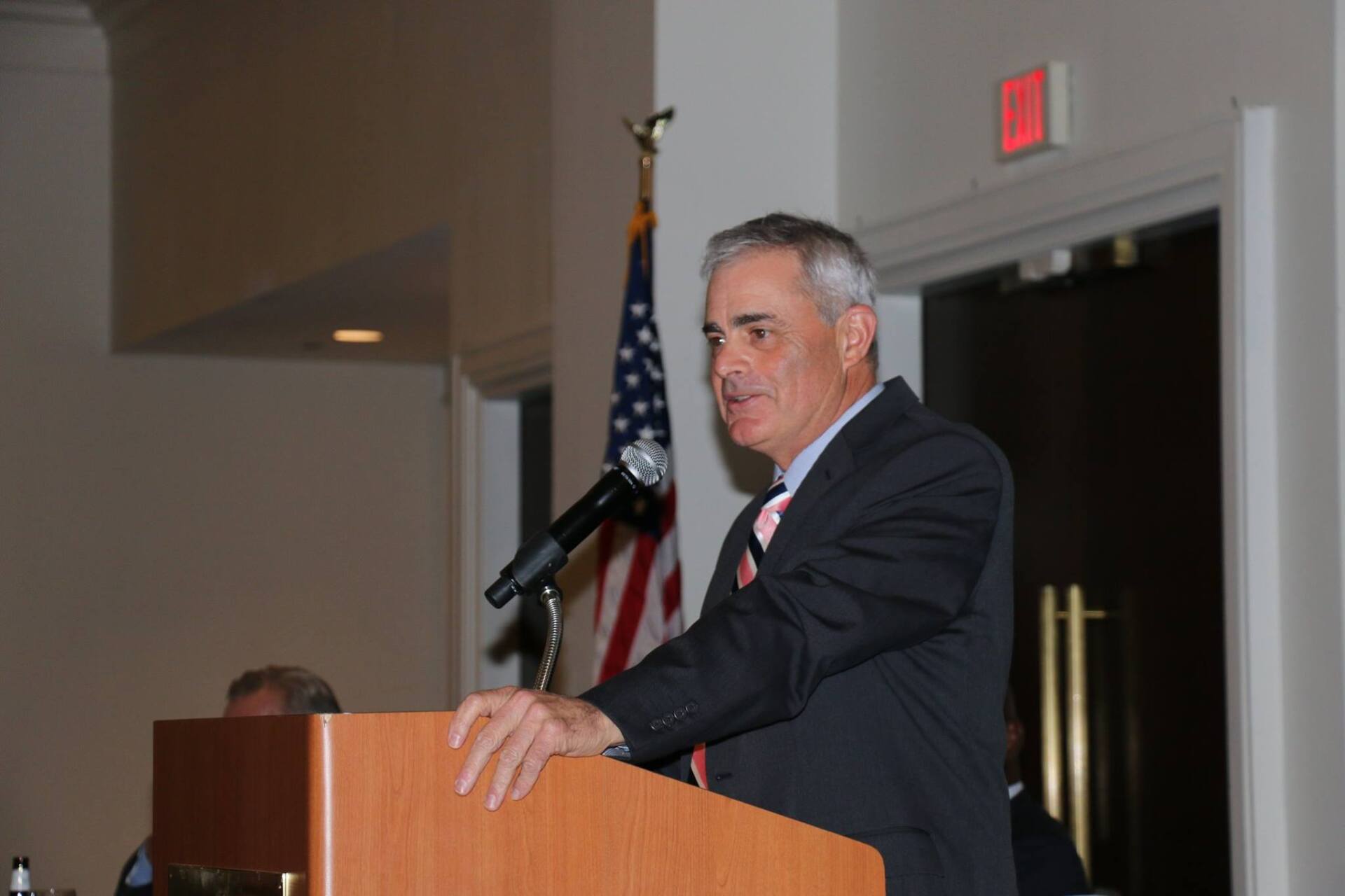 A man in a suit and tie is standing at a podium speaking into a microphone.