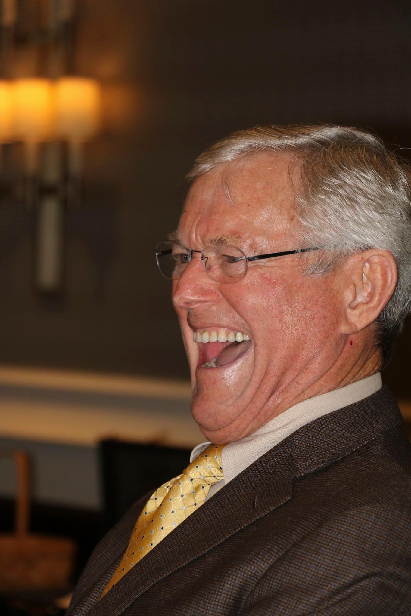 A man in a suit and tie is laughing with his mouth open.