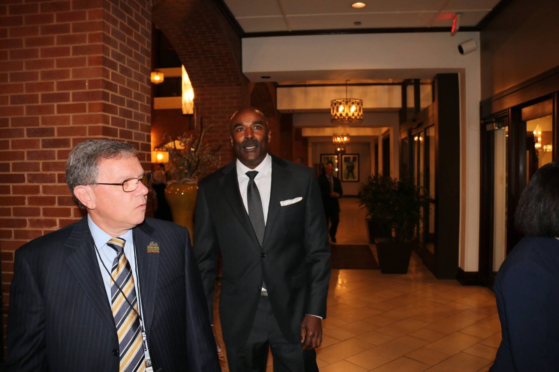 Two men in suits and ties are walking down a hallway