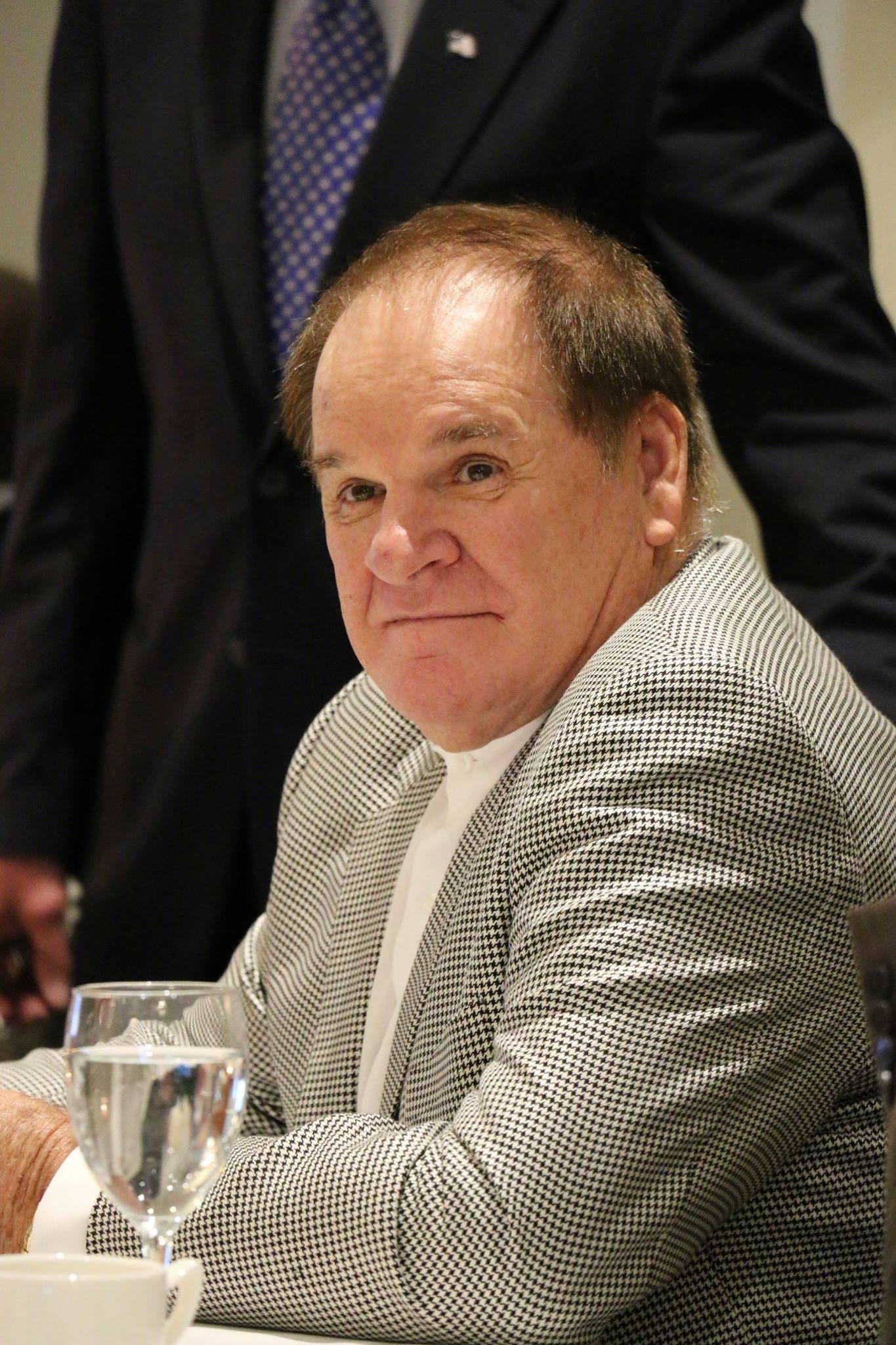 A man in a suit sits at a table with a glass of water