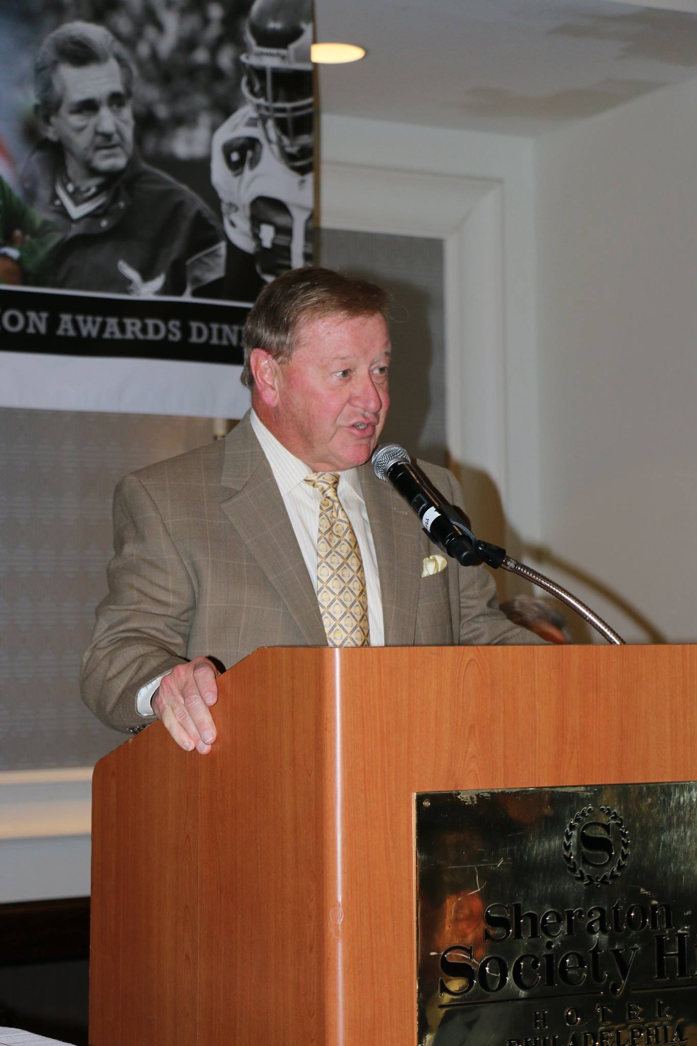 A man in a suit and tie stands at a podium speaking into a microphone