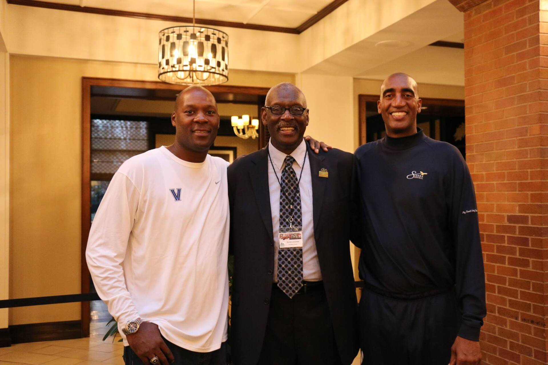 Three men are posing for a picture in a room with a brick wall