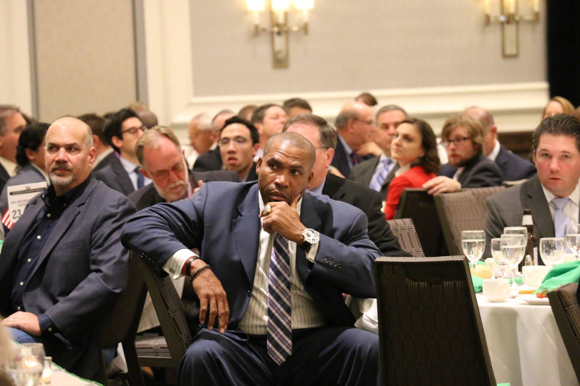 A man in a suit and tie is sitting in the audience at a conference.