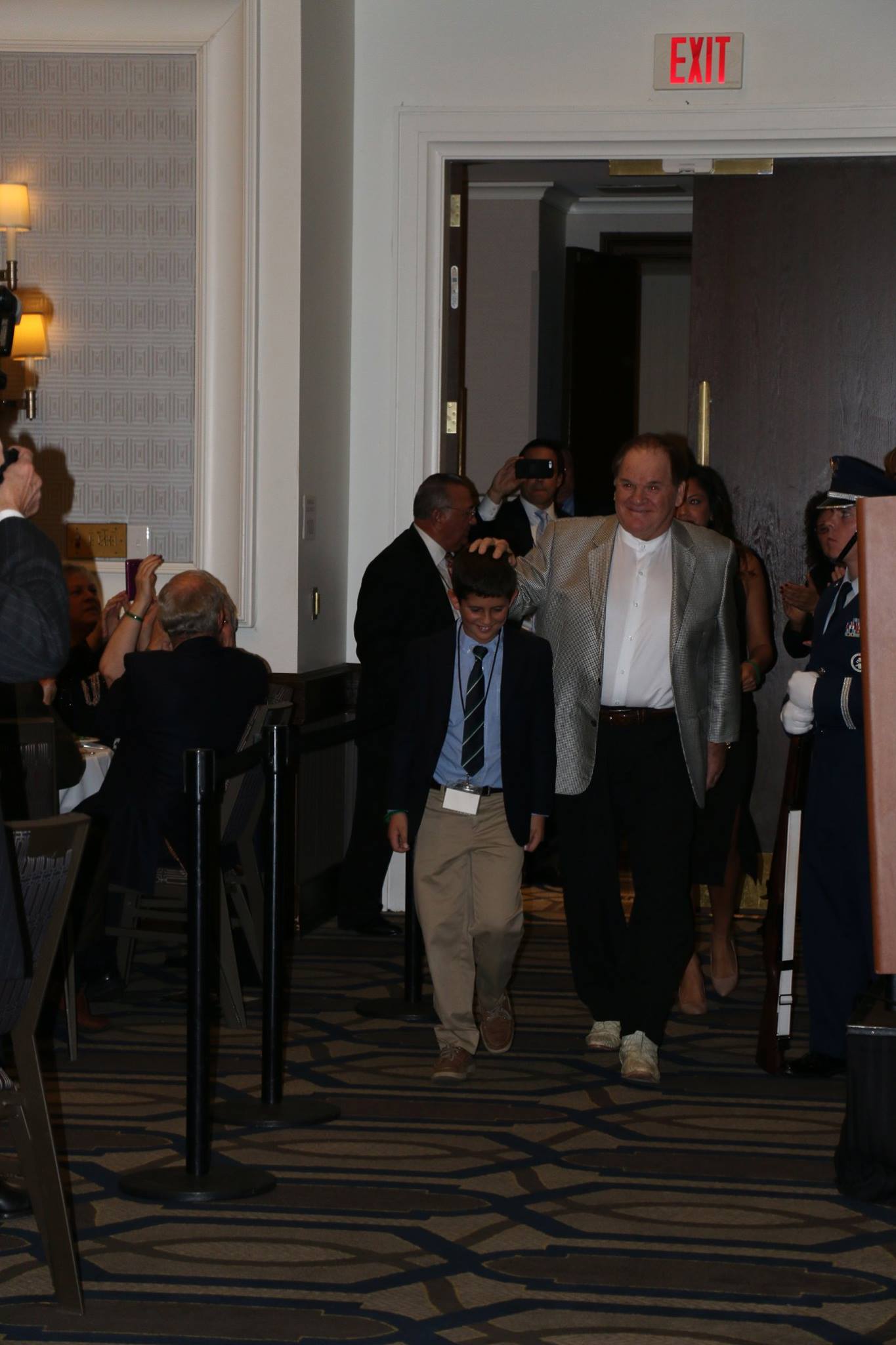 A group of people are walking down a hallway in front of an exit sign.