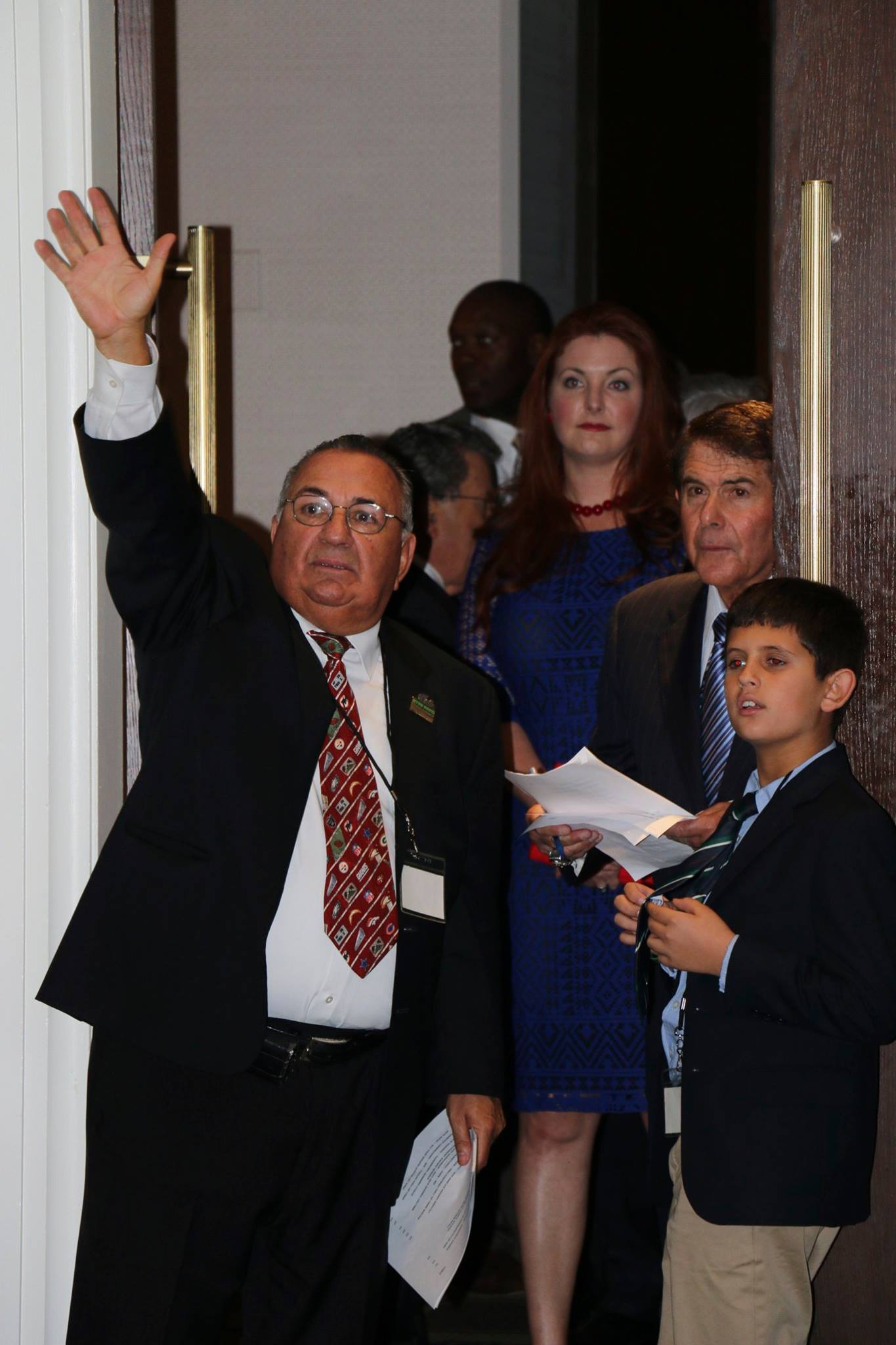 A man in a suit and tie is waving to a group of people