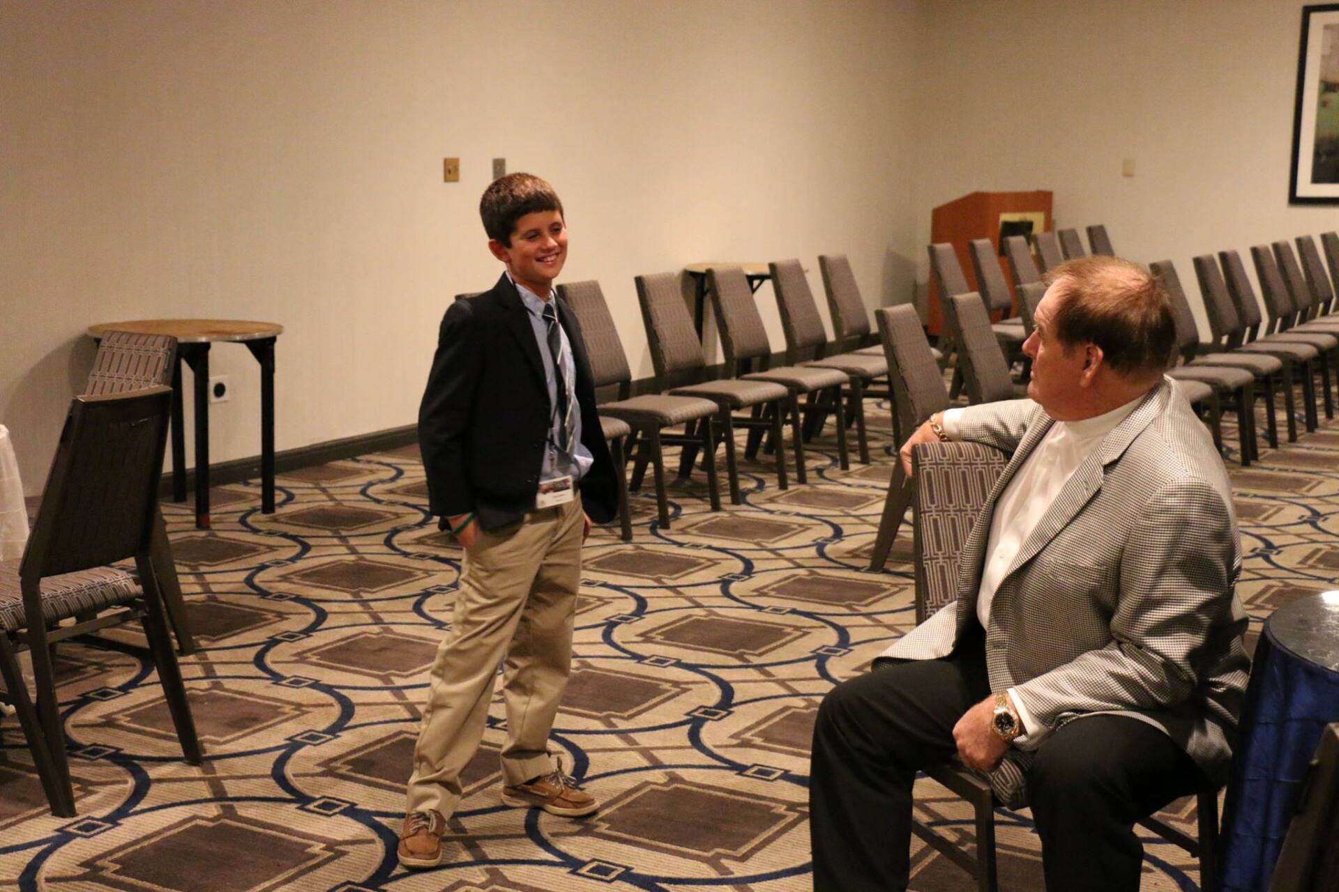 A man and a boy are standing in a room talking to each other.