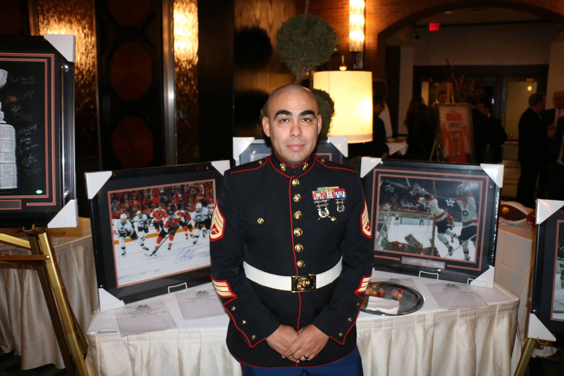 A man in a marine uniform is standing in front of a table with framed pictures on it.