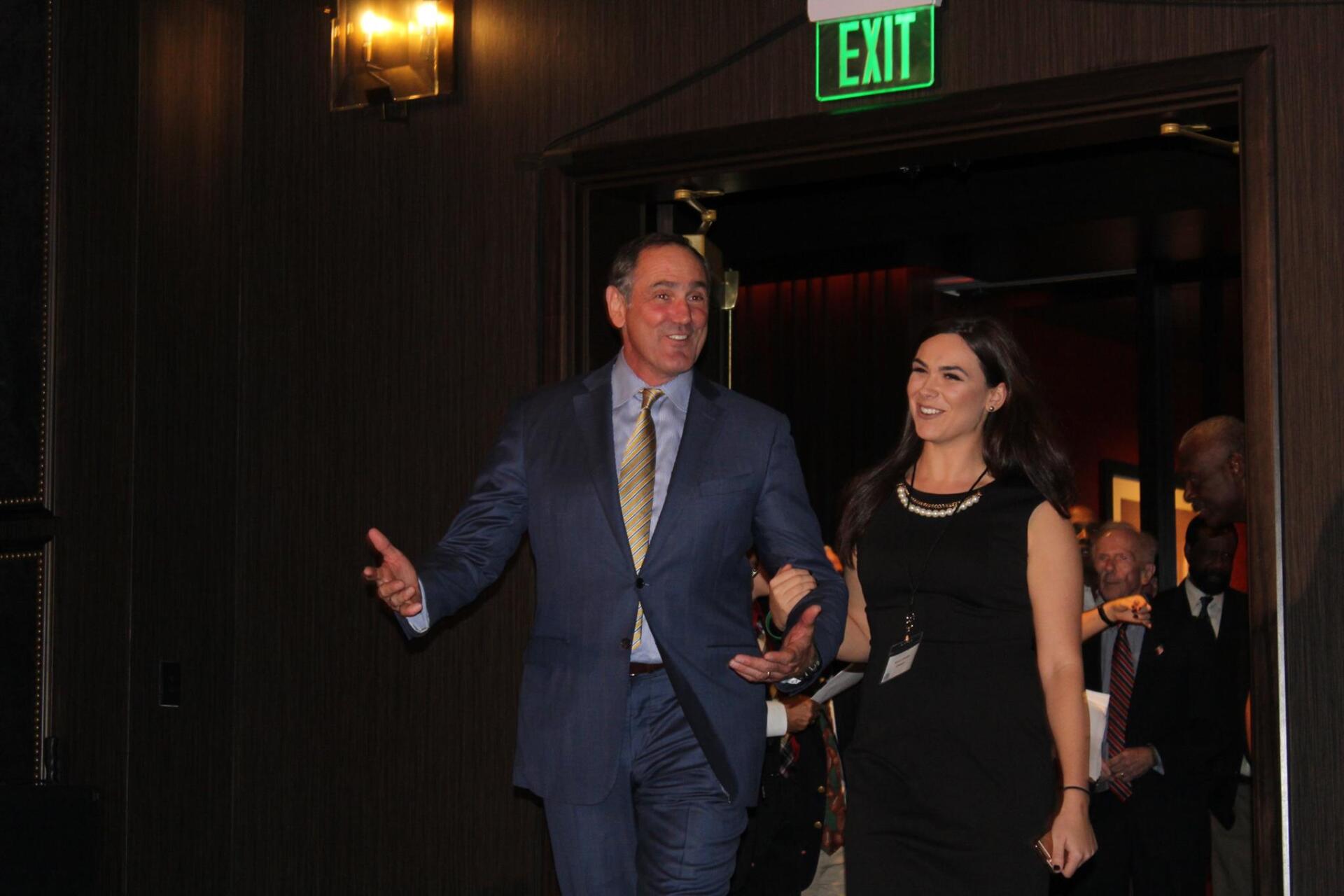 A man in a suit and tie is walking with a woman in a black dress.