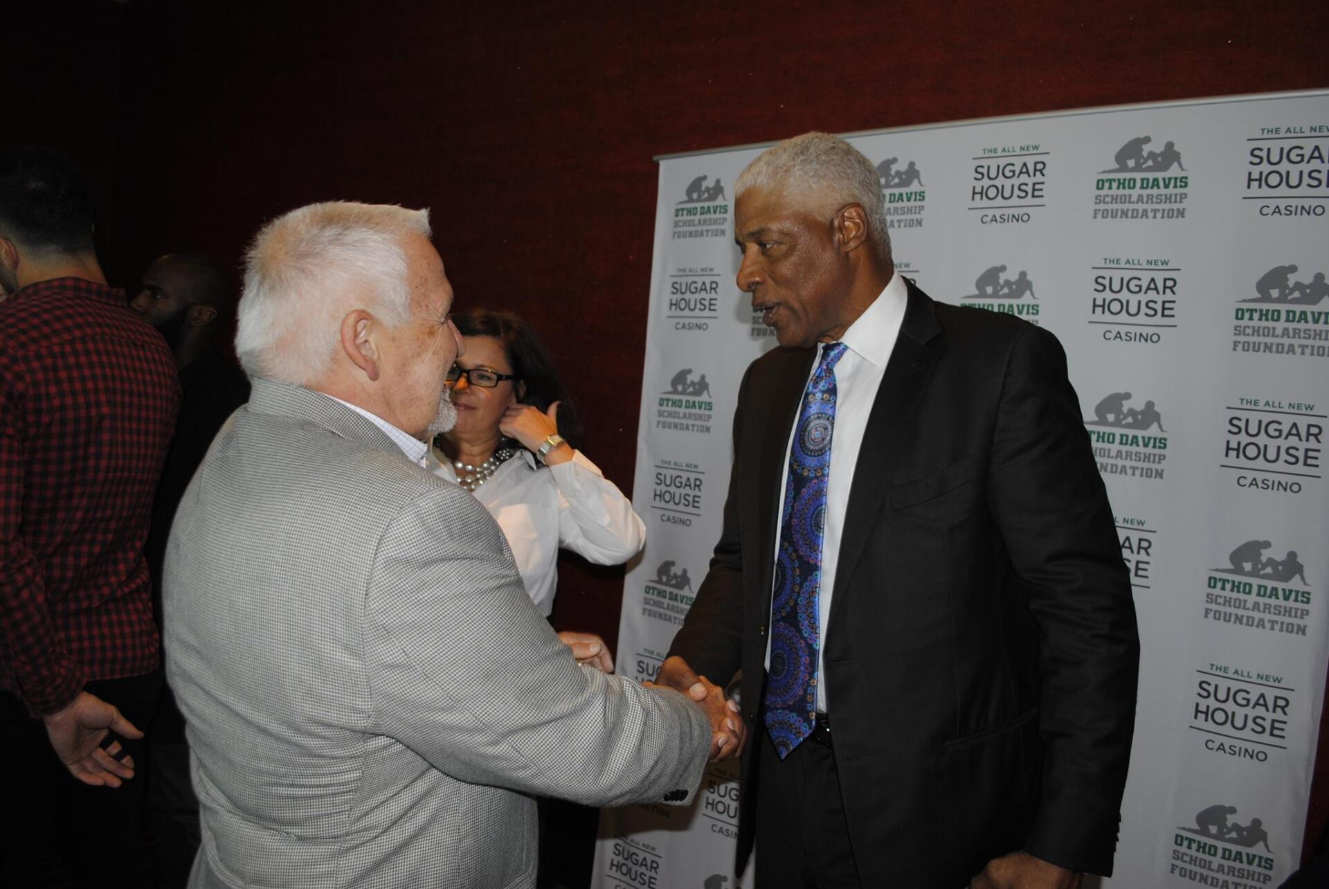 Two men are shaking hands in front of a sign that says sugar house