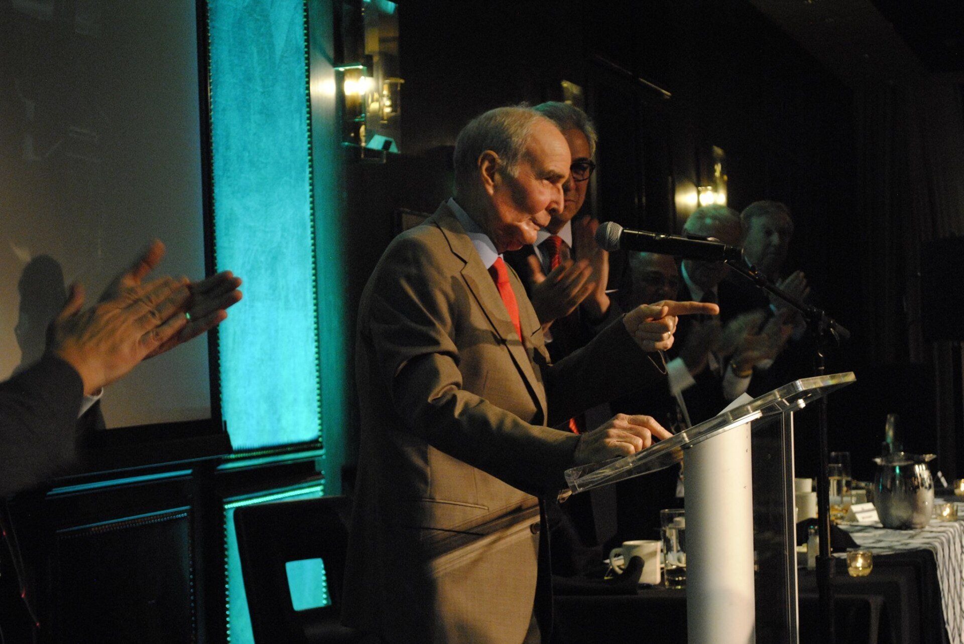 A man in a suit stands at a podium giving a speech