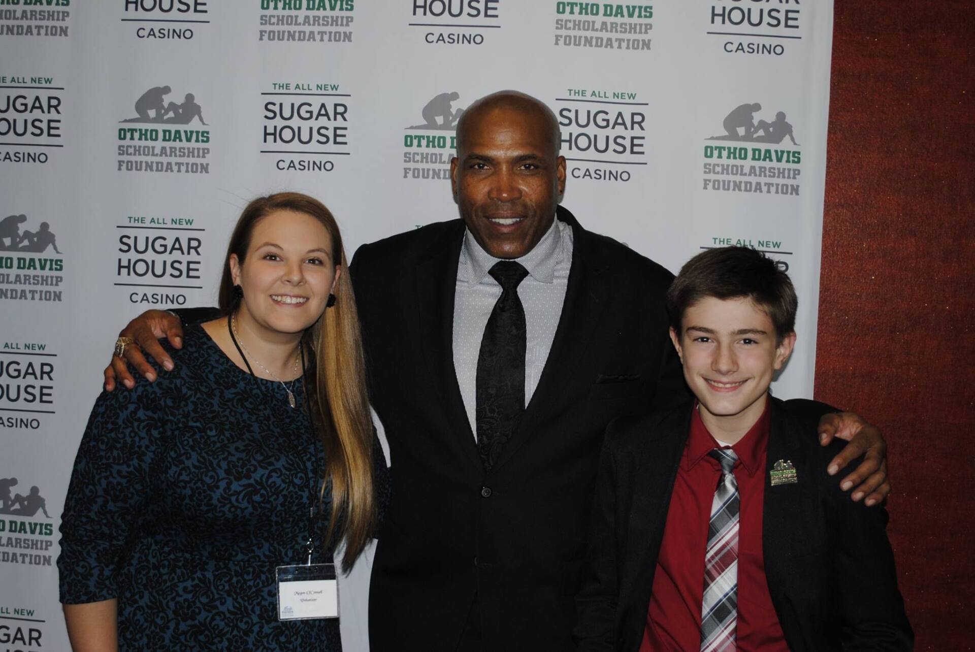 Three people pose for a picture in front of a sugar house banner