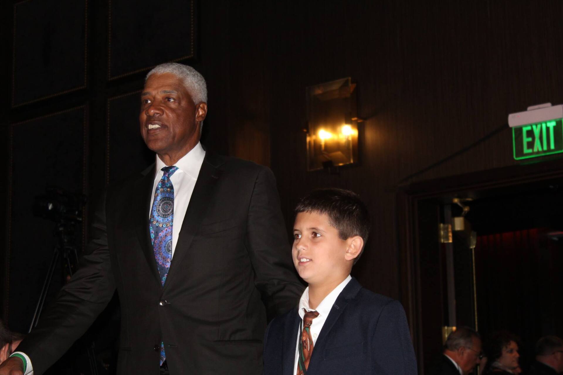 A man and a boy are walking in front of an exit sign