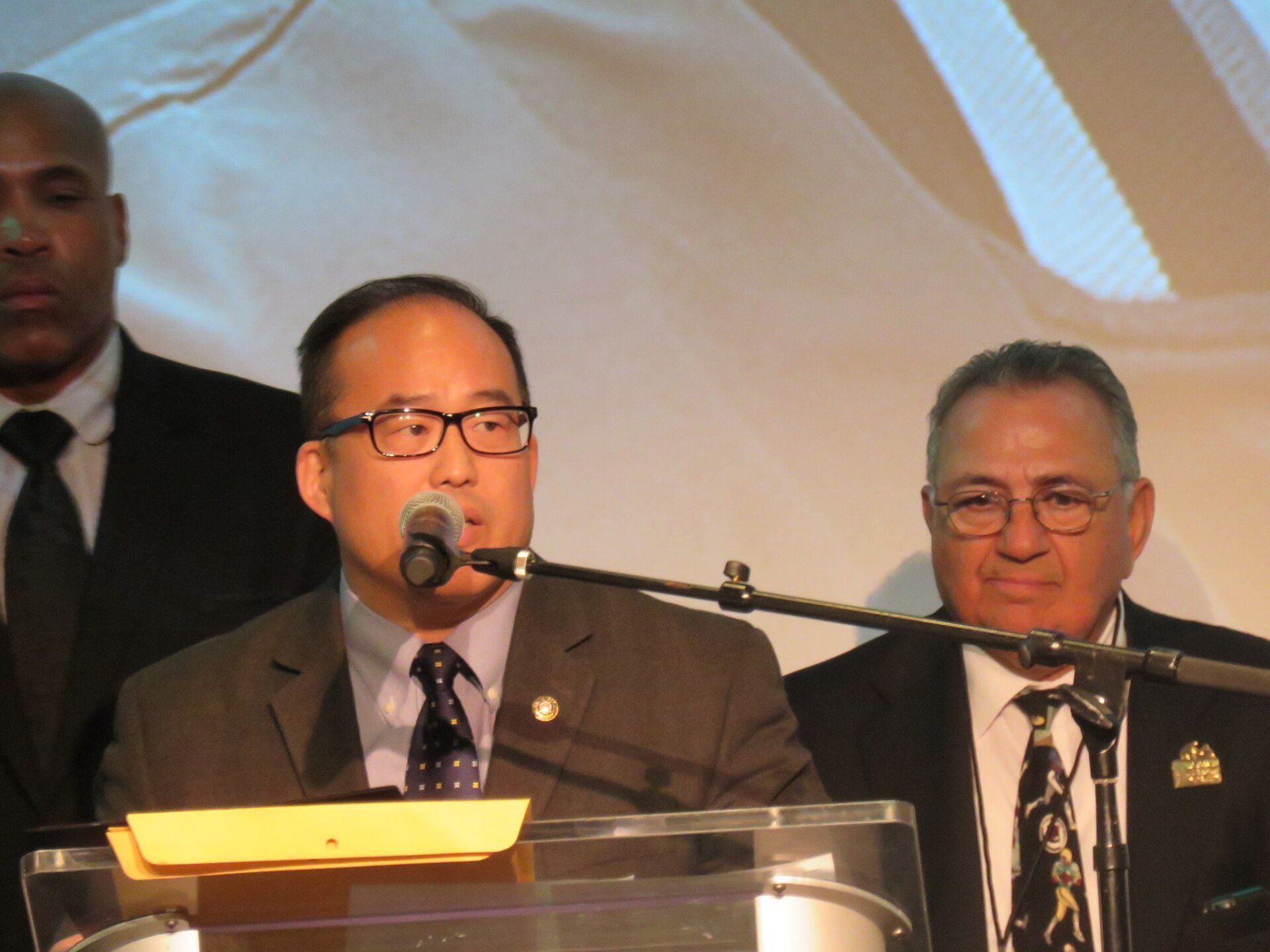 A man in a suit and tie is speaking into a microphone