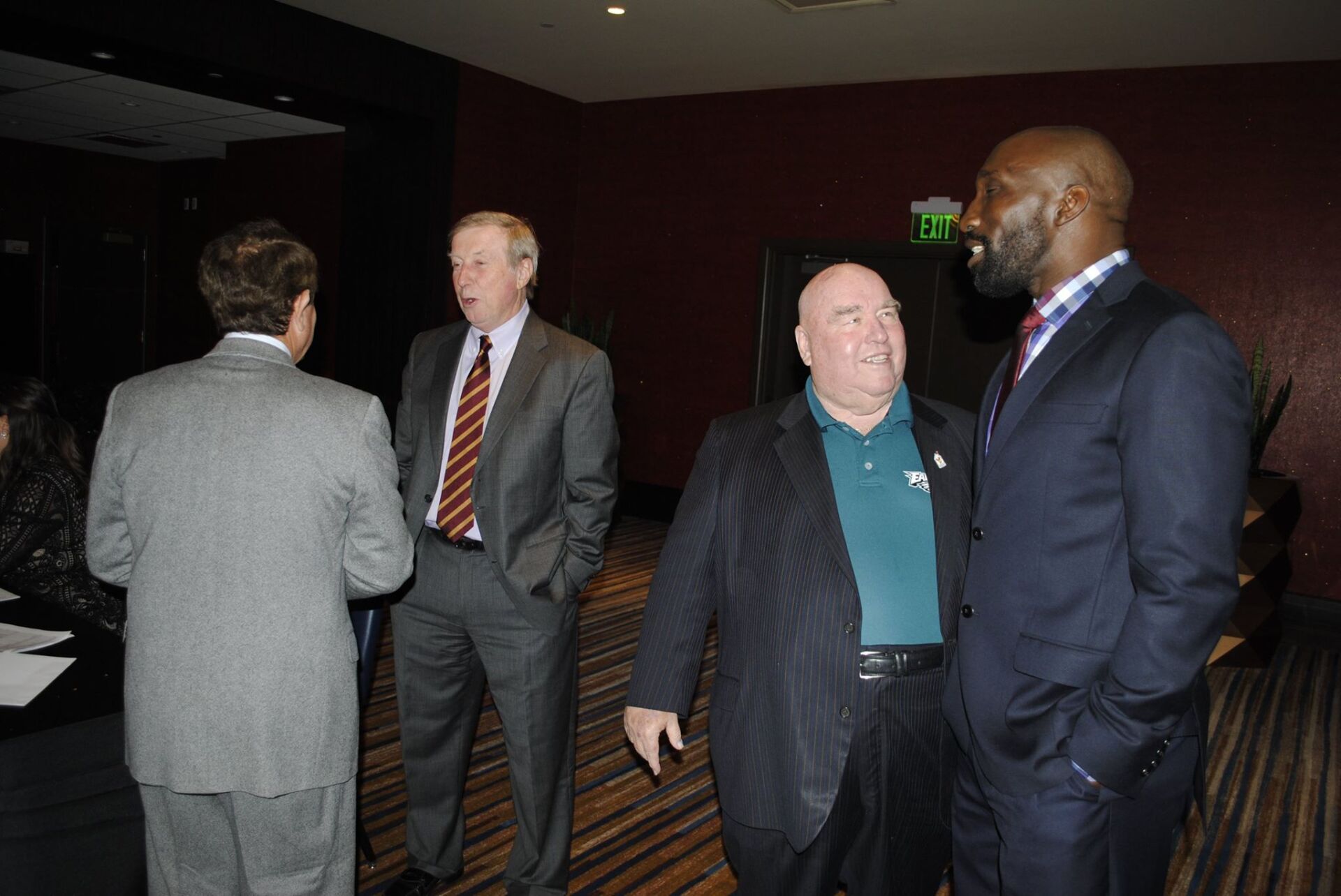 A group of men in suits are standing in a room talking to each other