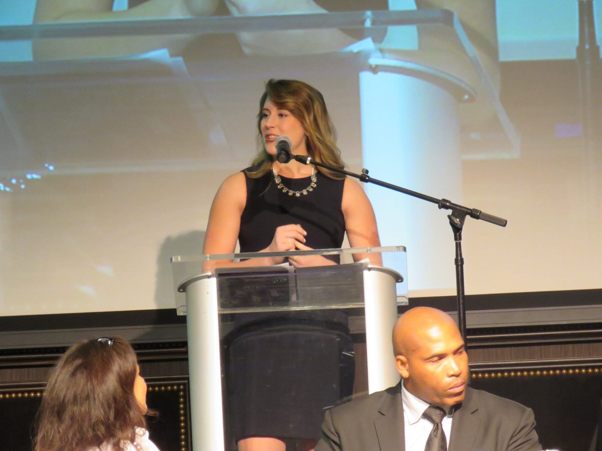 A woman stands at a podium speaking into a microphone