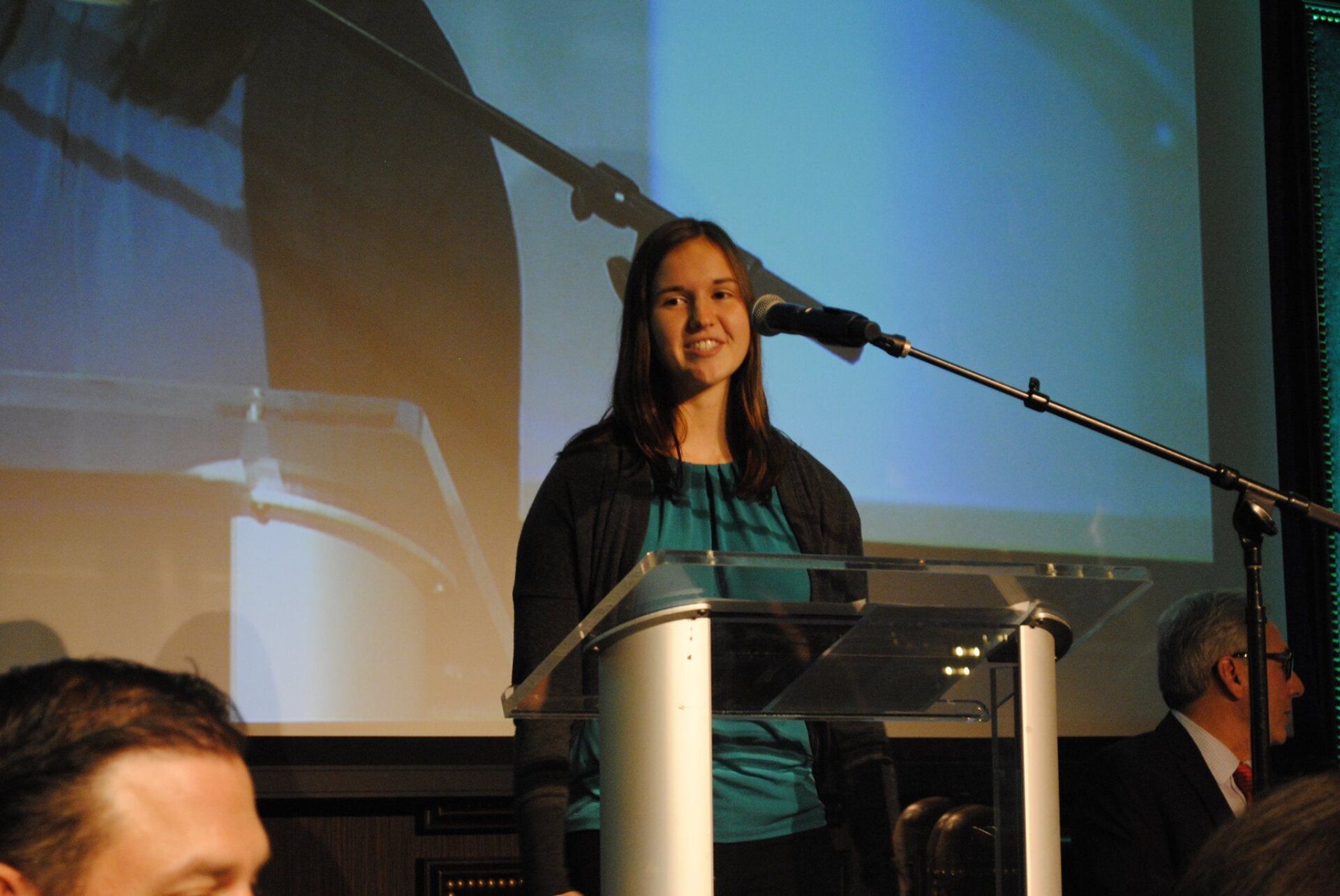 A woman stands at a podium speaking into a microphone