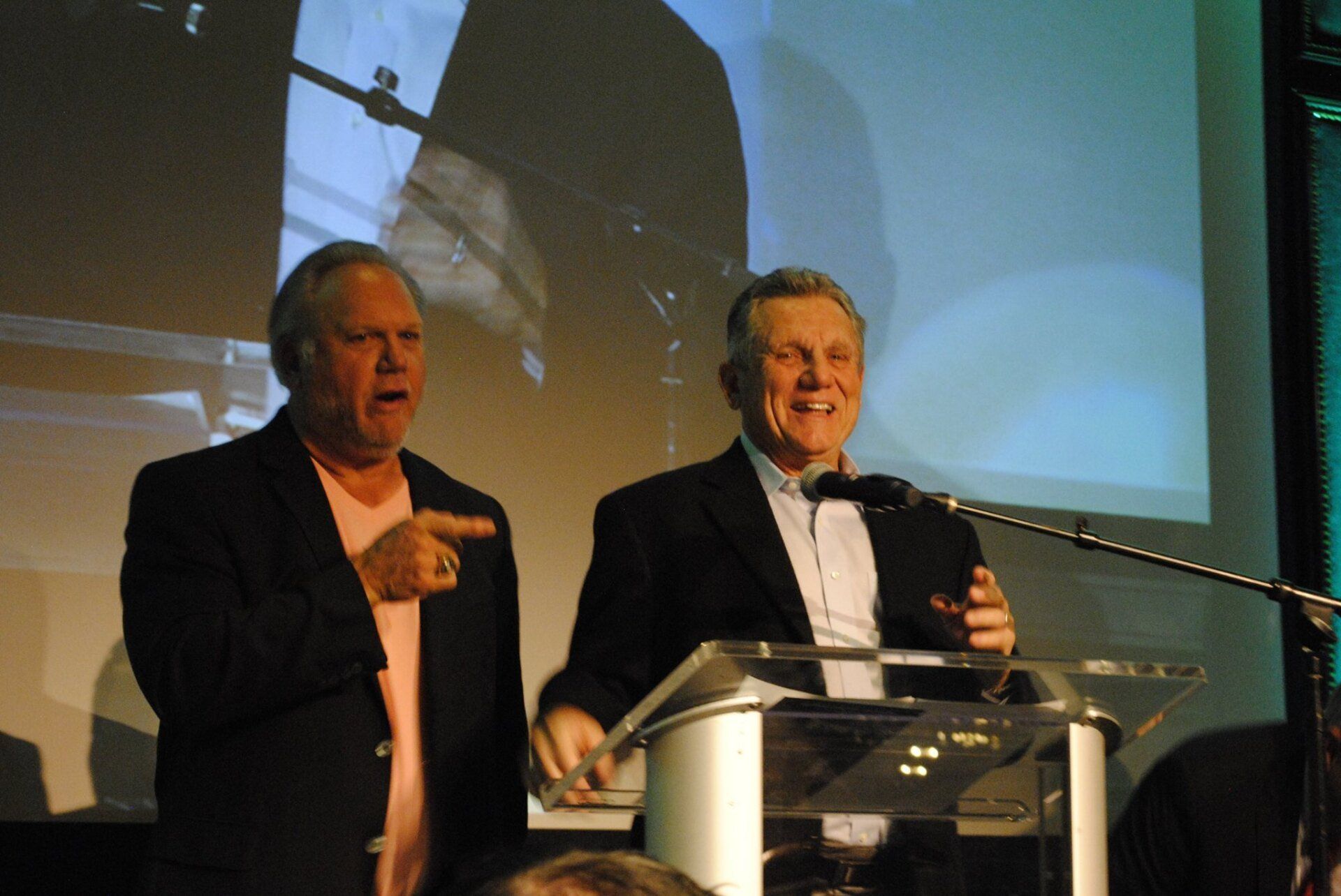Two men standing at a podium with one pointing at the camera