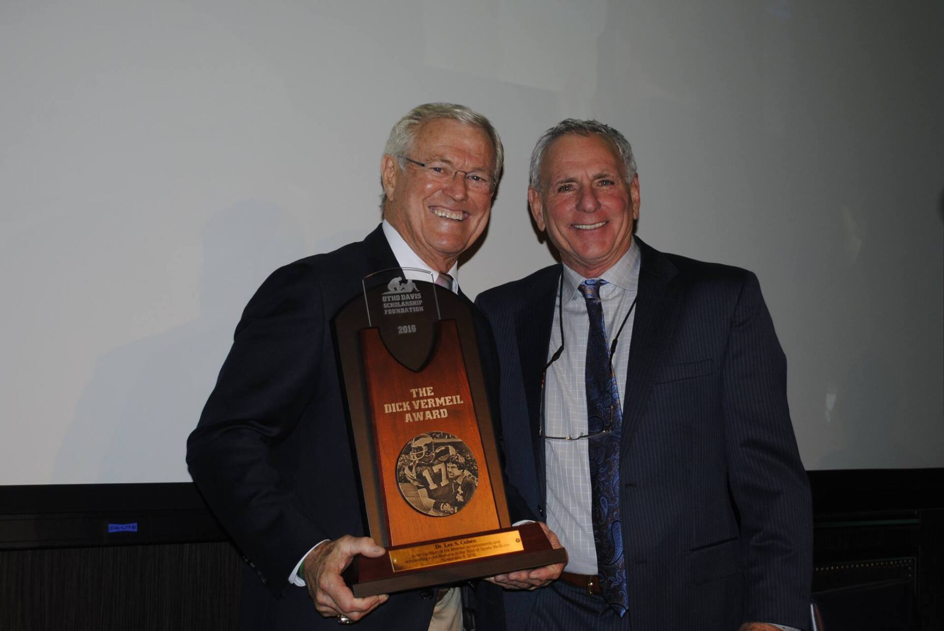 Two men in suits are holding a trophy and smiling
