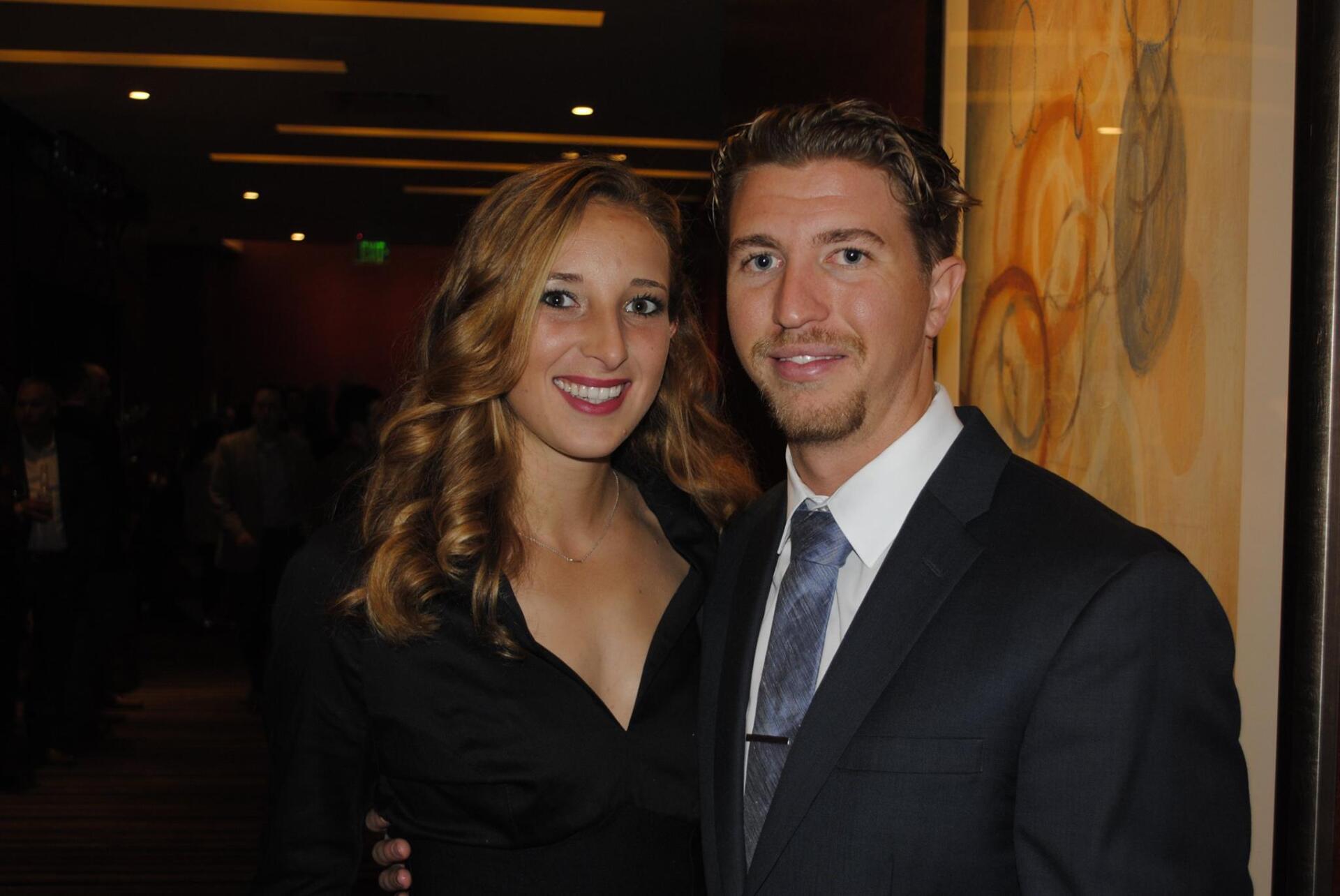 A man in a suit and tie poses with a woman in a black dress