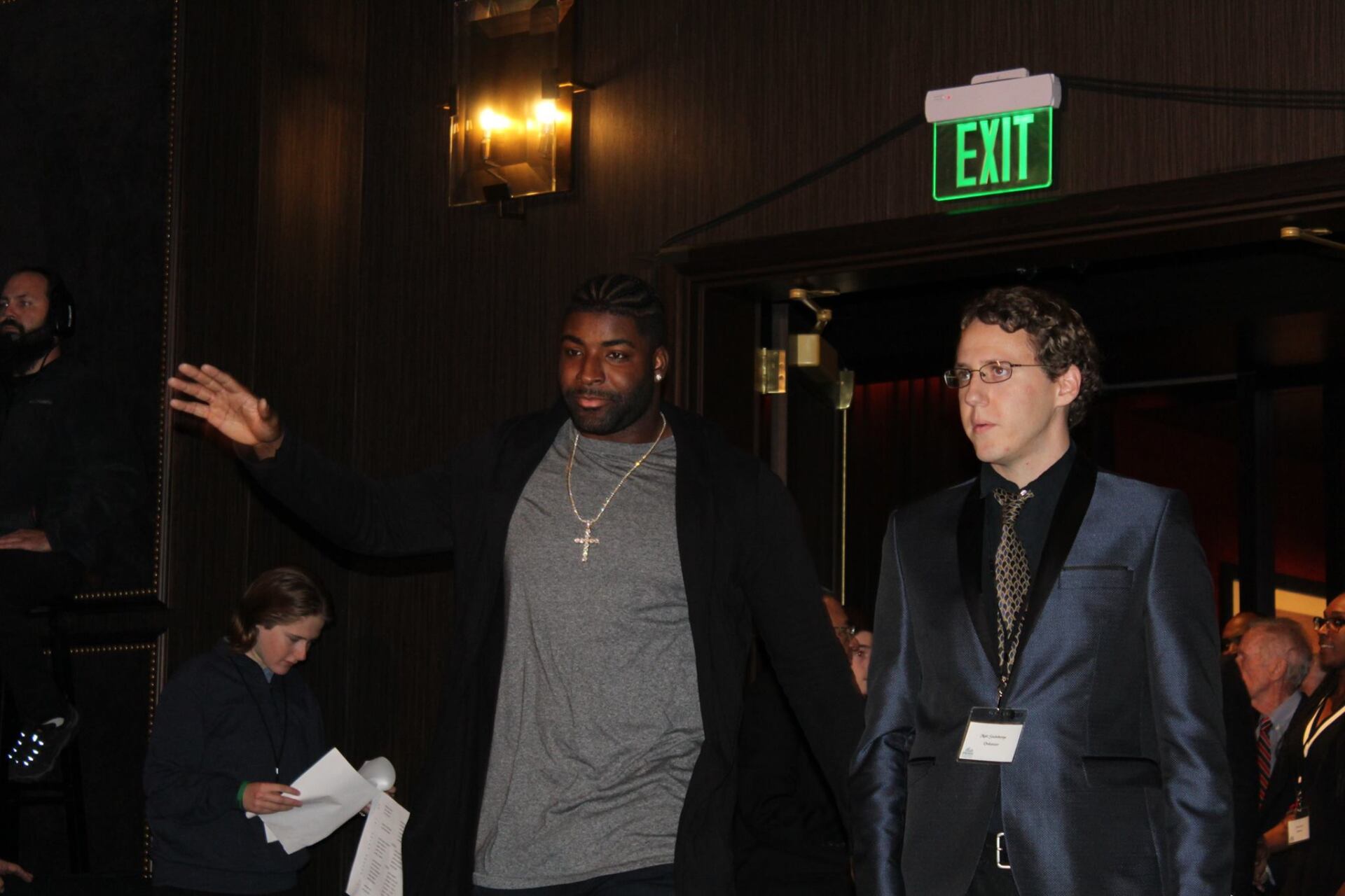Two men are walking in front of an exit sign