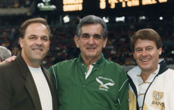 Three men posing for a picture with one wearing a saints jacket