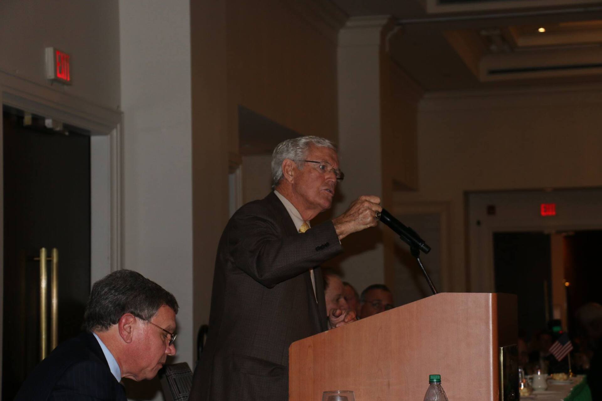 A man in a suit is standing at a podium talking into a microphone.