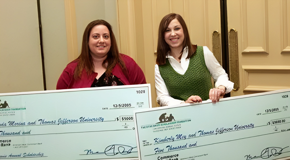 Two women are holding large checks in their hands.