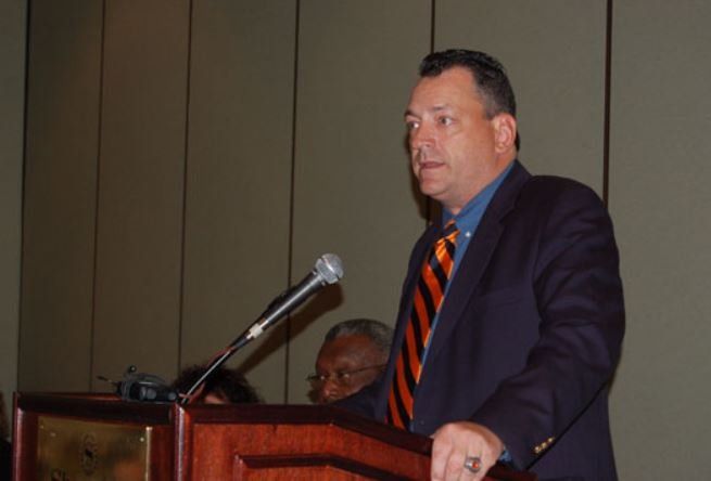A man in a suit and tie is speaking into a microphone