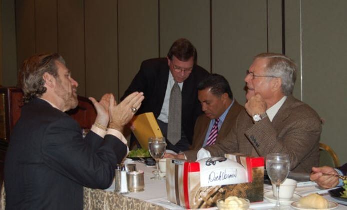 A group of men are sitting at a table with a sign that says ' catering ' on it