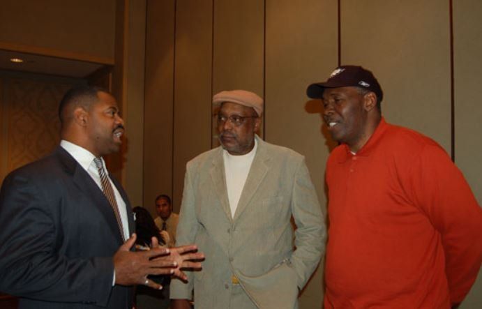 Three men are standing in a room talking to each other