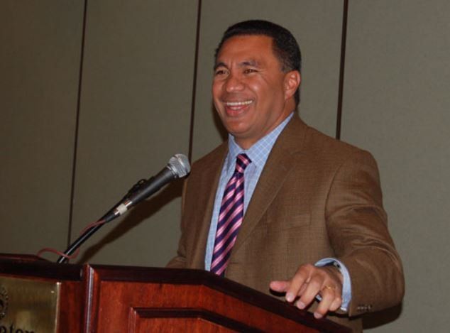 A man in a suit and tie is speaking into a microphone