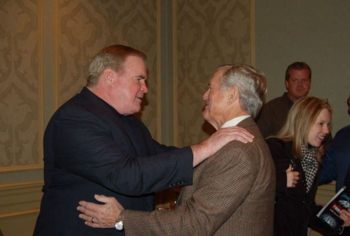 Two men in suits are hugging each other in a room