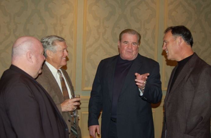 A group of men are standing in a room talking to each other