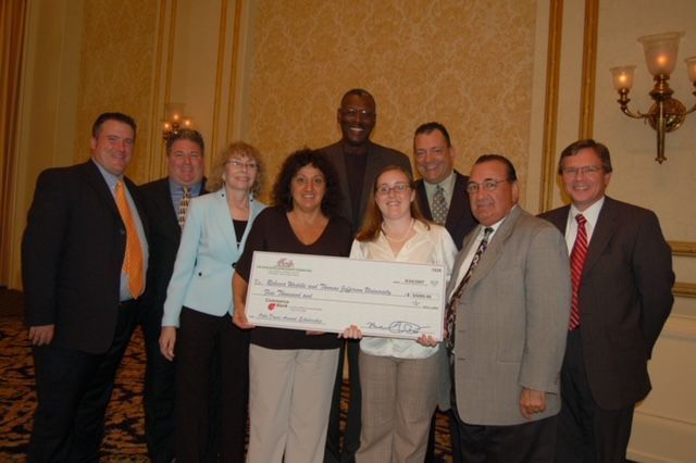 A group of people posing for a picture with a woman holding a large check