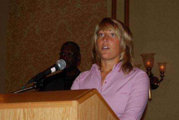 A woman in a pink shirt is speaking into a microphone