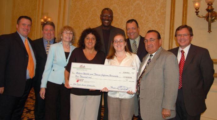 A group of people standing around a woman holding a large check