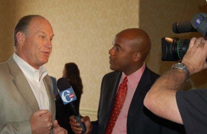 A man in a suit is talking to another man in a pink shirt