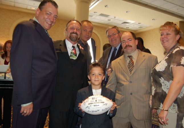 A group of people standing around a young boy holding a football