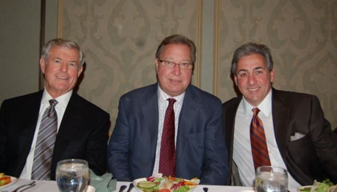 Three men in suits and ties are sitting at a table with plates of food.